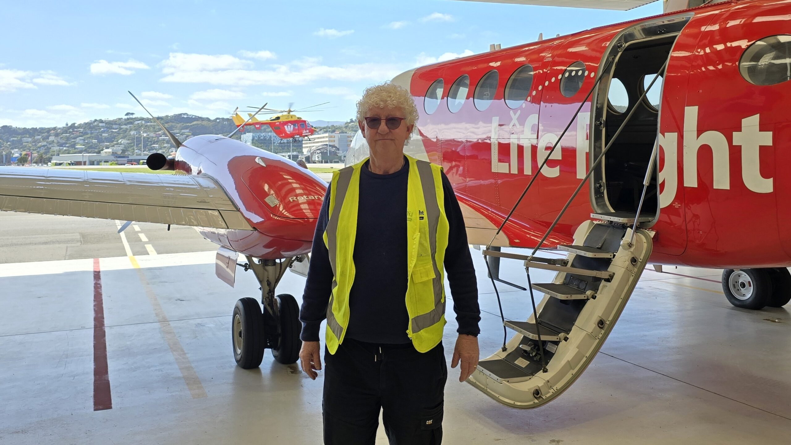Paul standing in front of Life Flight Air Ambulance Plane with Life Flight Westpac Rescue Helicopter flying in background.